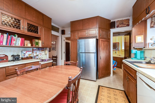 kitchen with white dishwasher, sink, decorative backsplash, and stainless steel fridge