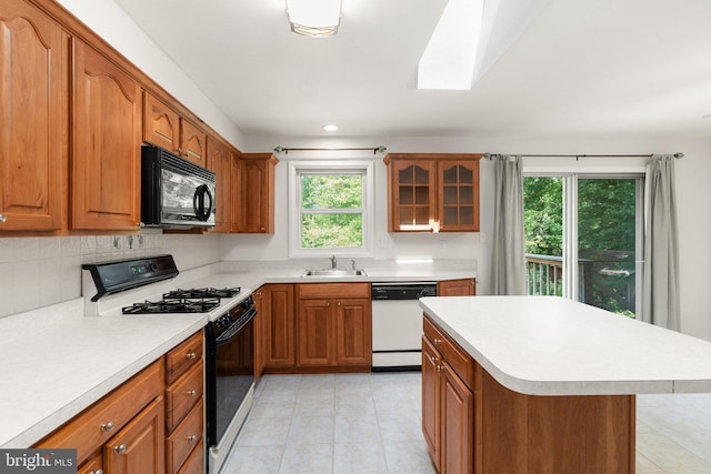 kitchen featuring range with gas stovetop, a skylight, sink, backsplash, and white dishwasher