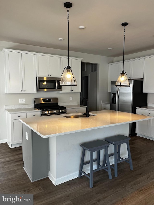 kitchen with appliances with stainless steel finishes, dark wood-type flooring, white cabinetry, and hanging light fixtures