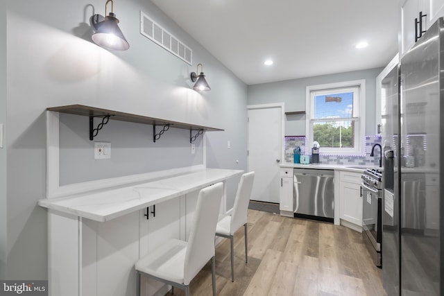 kitchen with white cabinetry, light stone countertops, stainless steel appliances, and a kitchen bar