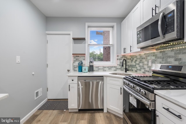 kitchen with sink, stainless steel appliances, white cabinets, and light wood-type flooring