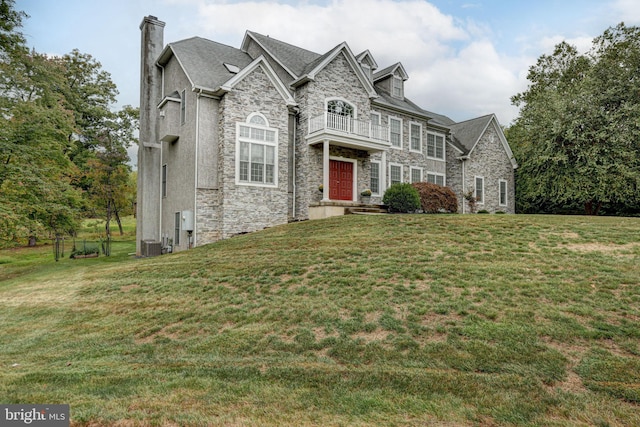 view of front facade with a chimney, stone siding, a front yard, and a balcony