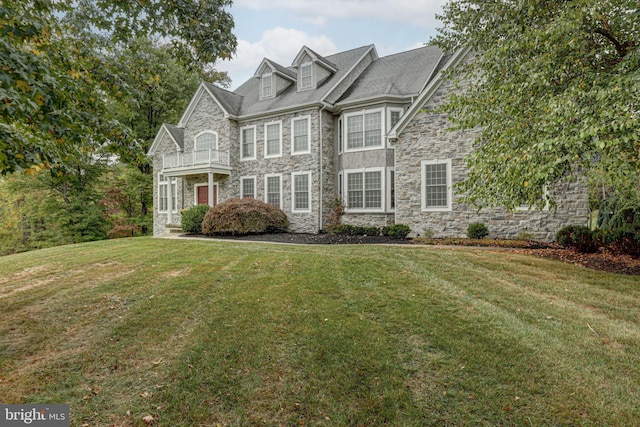 view of front of property featuring stone siding, a balcony, and a front yard