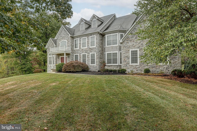 view of front of home with stone siding, a balcony, and a front lawn