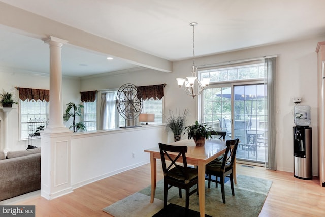 dining area with light wood-type flooring, crown molding, an inviting chandelier, and ornate columns