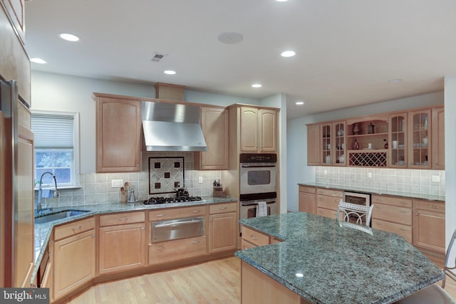 kitchen featuring wall chimney exhaust hood, a center island, stone countertops, and sink