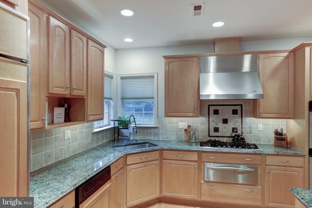 kitchen with light stone counters, light brown cabinets, sink, wall chimney range hood, and dishwashing machine