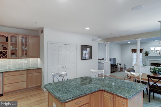 kitchen with light hardwood / wood-style floors, tasteful backsplash, a kitchen island, dark stone countertops, and ornate columns