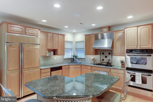 kitchen with wall chimney exhaust hood, stainless steel appliances, a kitchen island, and dark stone counters