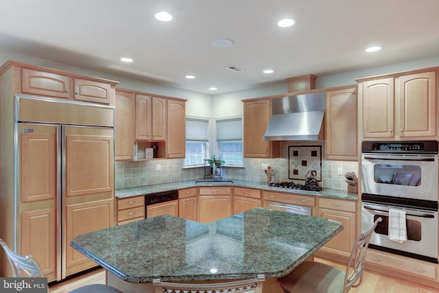 kitchen with paneled appliances, a sink, wall chimney exhaust hood, and light brown cabinetry