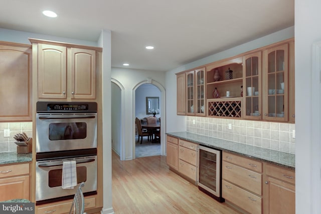 kitchen featuring dark stone counters, wine cooler, double oven, and light hardwood / wood-style flooring