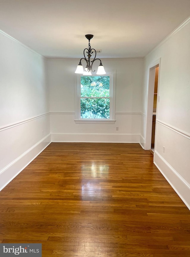 spare room featuring hardwood / wood-style floors, an inviting chandelier, and ornamental molding