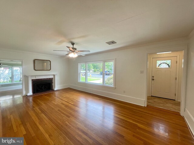 unfurnished living room featuring hardwood / wood-style floors, ornamental molding, ceiling fan, and a brick fireplace