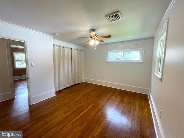 unfurnished room with a wealth of natural light, dark wood finished floors, visible vents, and baseboards