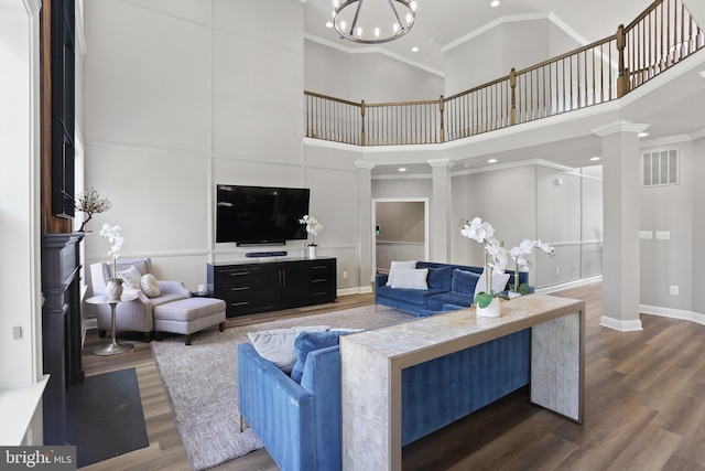 living area featuring ornate columns, visible vents, dark wood-style flooring, and ornamental molding