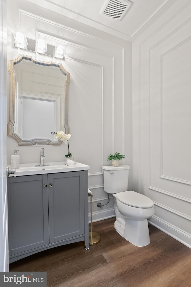 bathroom with visible vents, a decorative wall, toilet, vanity, and wood finished floors