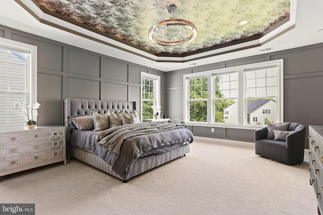 bedroom with light carpet, a tray ceiling, and a decorative wall