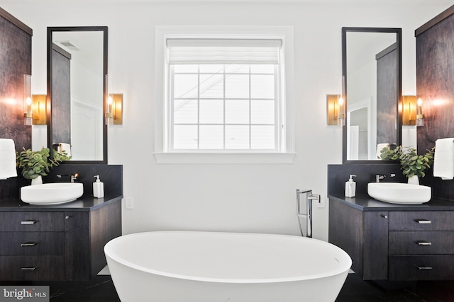 full bath with two vanities, a soaking tub, and a sink