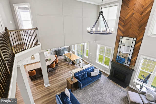 living area with a decorative wall, a notable chandelier, wood finished floors, a fireplace with flush hearth, and a towering ceiling