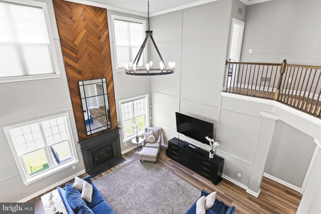 living room featuring a notable chandelier, a high ceiling, a fireplace with flush hearth, wood finished floors, and baseboards