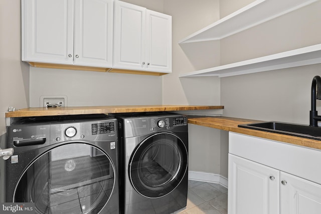 laundry area with cabinet space, light tile patterned floors, baseboards, washing machine and clothes dryer, and a sink