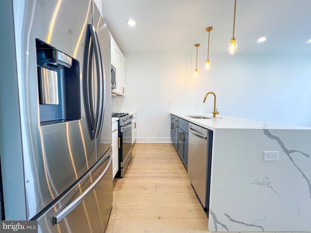 kitchen featuring white cabinetry, stainless steel appliances, hanging light fixtures, sink, and light hardwood / wood-style flooring