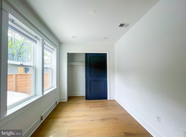 unfurnished bedroom with light hardwood / wood-style floors, multiple windows, and a closet