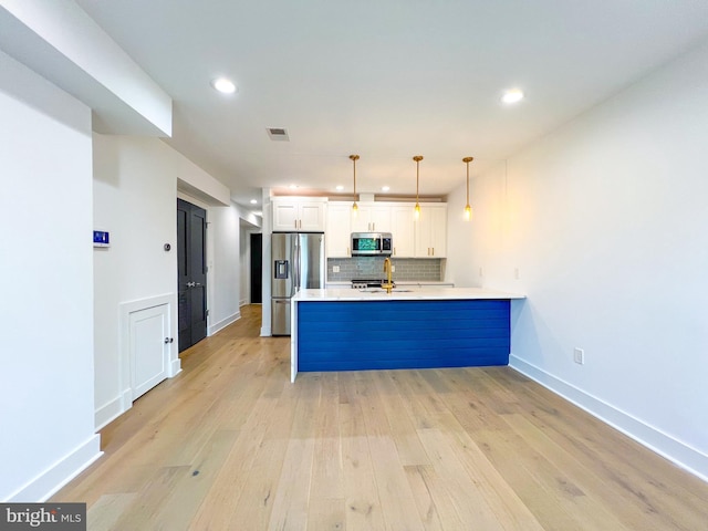 kitchen featuring tasteful backsplash, light wood-type flooring, kitchen peninsula, white cabinets, and appliances with stainless steel finishes