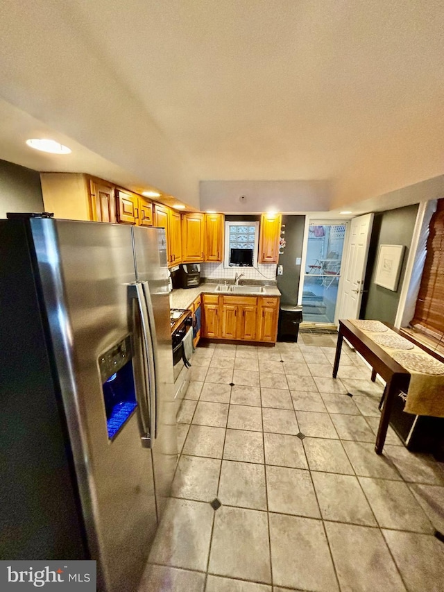 kitchen with sink, stainless steel fridge with ice dispenser, light tile patterned floors, decorative backsplash, and stove