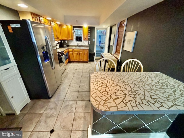 kitchen featuring gas range, sink, light tile patterned floors, and stainless steel fridge