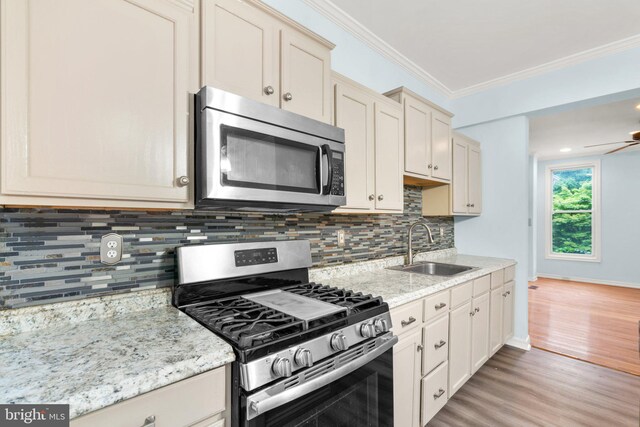 kitchen featuring sink, crown molding, appliances with stainless steel finishes, cream cabinets, and light hardwood / wood-style floors