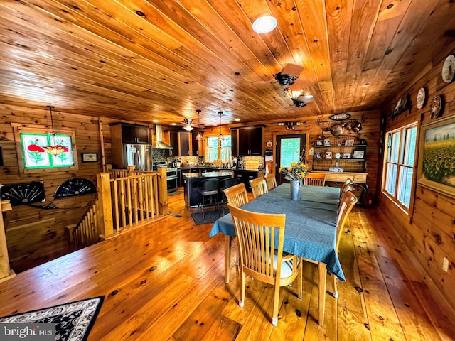 dining space featuring wooden walls, rustic walls, wood ceiling, ceiling fan, and light hardwood / wood-style floors