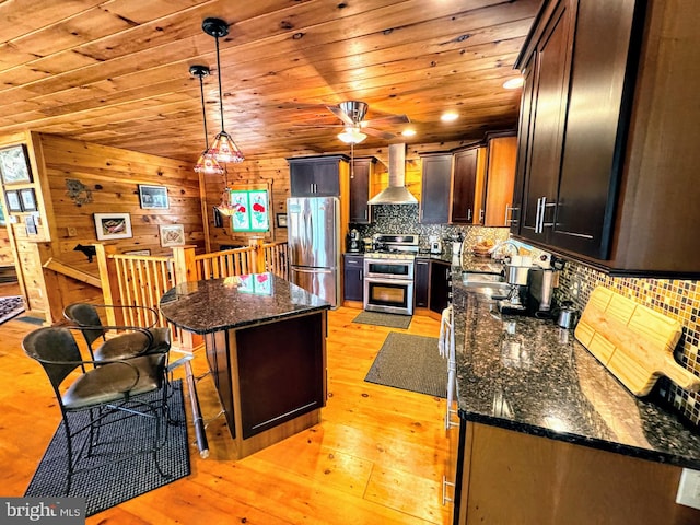 kitchen with stainless steel fridge, wall chimney range hood, double oven range, light hardwood / wood-style floors, and a kitchen island