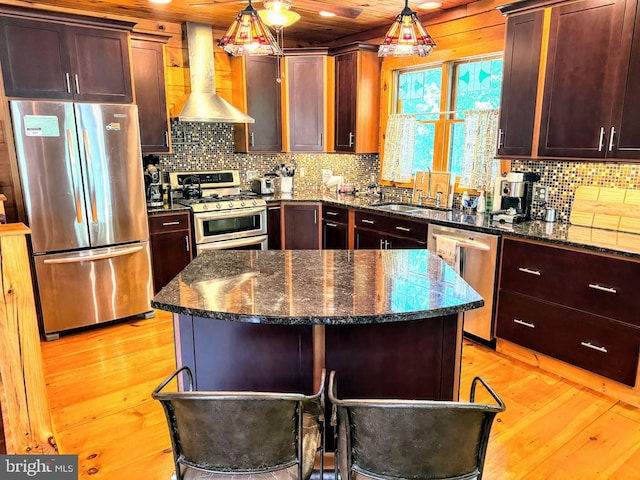 kitchen with stainless steel appliances, light hardwood / wood-style floors, dark stone countertops, and wall chimney range hood