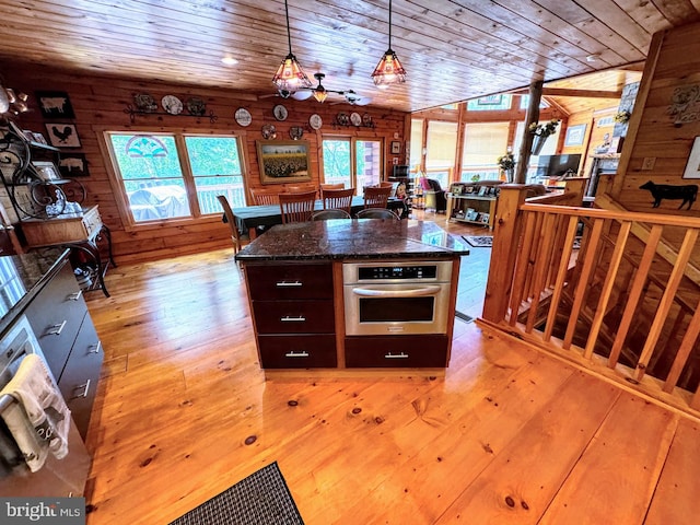 kitchen with lofted ceiling, wood walls, oven, and light hardwood / wood-style flooring