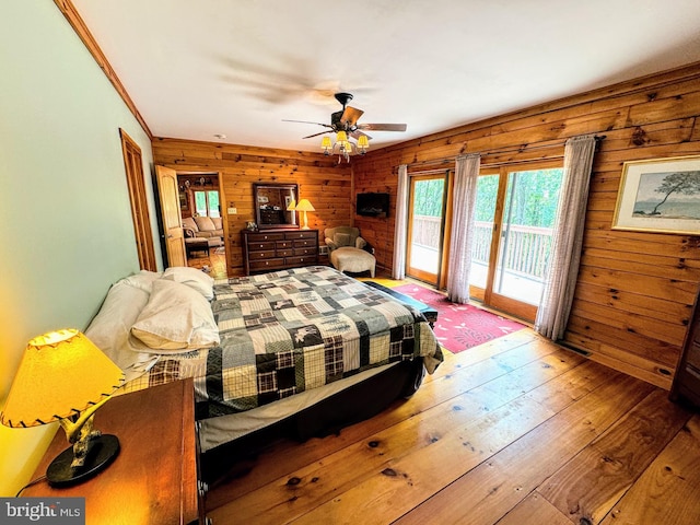 bedroom featuring wood-type flooring, wood walls, access to outside, and ceiling fan