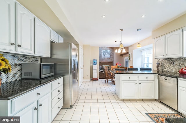 kitchen with hanging light fixtures, white cabinets, stainless steel appliances, and a brick fireplace