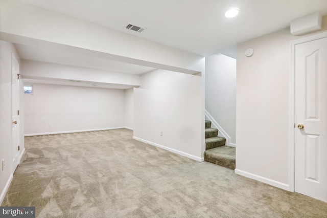 finished below grade area with visible vents, light carpet, stairway, and baseboards