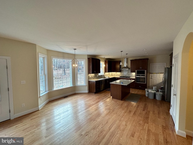 kitchen with a kitchen island, pendant lighting, decorative backsplash, dark brown cabinetry, and wall chimney range hood