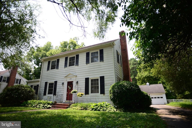 colonial inspired home featuring a garage, an outbuilding, and a front lawn