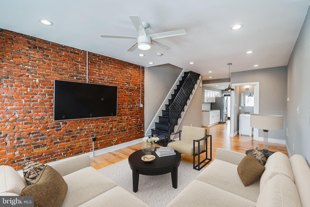 living room featuring ceiling fan, brick wall, and light hardwood / wood-style floors