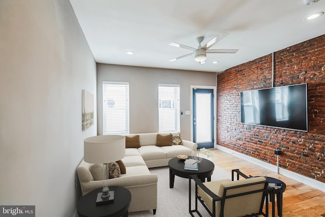 living room featuring wood-type flooring, brick wall, and ceiling fan