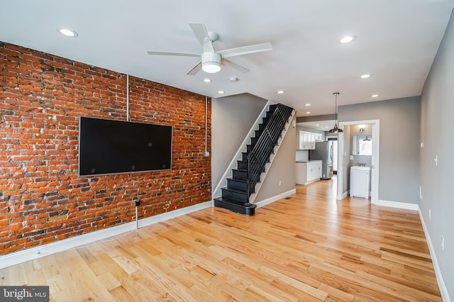 unfurnished living room with ceiling fan, brick wall, and light hardwood / wood-style flooring