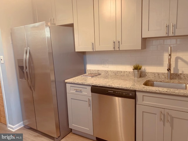 kitchen featuring appliances with stainless steel finishes, light stone countertops, sink, and decorative backsplash