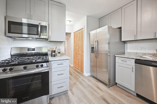 kitchen with backsplash, appliances with stainless steel finishes, light stone countertops, light wood-type flooring, and sink