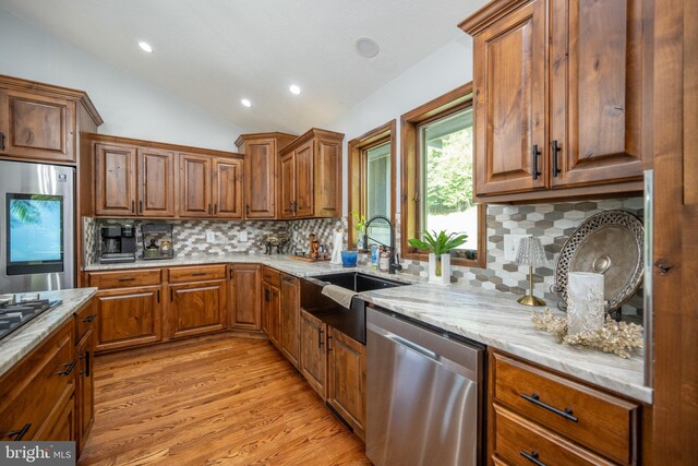 kitchen featuring light wood-type flooring, dishwasher, light stone countertops, vaulted ceiling, and backsplash