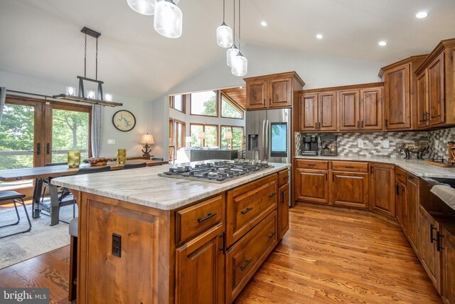 kitchen featuring stainless steel appliances, light stone counters, backsplash, light hardwood / wood-style floors, and lofted ceiling