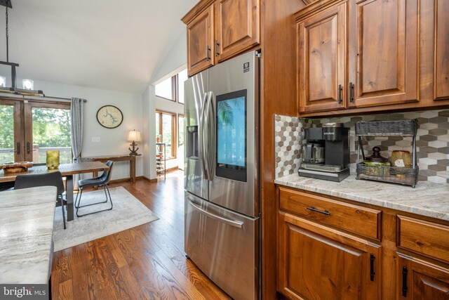 kitchen with decorative backsplash, wood-type flooring, light stone countertops, and stainless steel refrigerator with ice dispenser