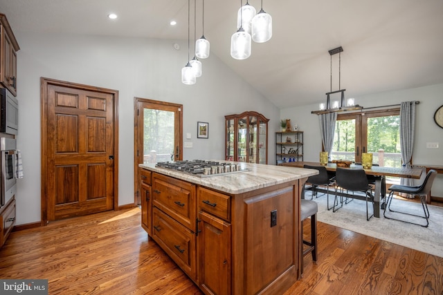 kitchen with a kitchen island, appliances with stainless steel finishes, wood-type flooring, and decorative light fixtures