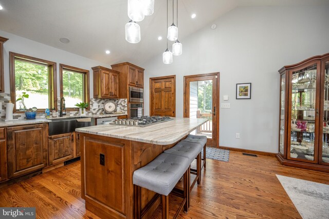 kitchen with hanging light fixtures, decorative backsplash, a kitchen island, light hardwood / wood-style floors, and appliances with stainless steel finishes